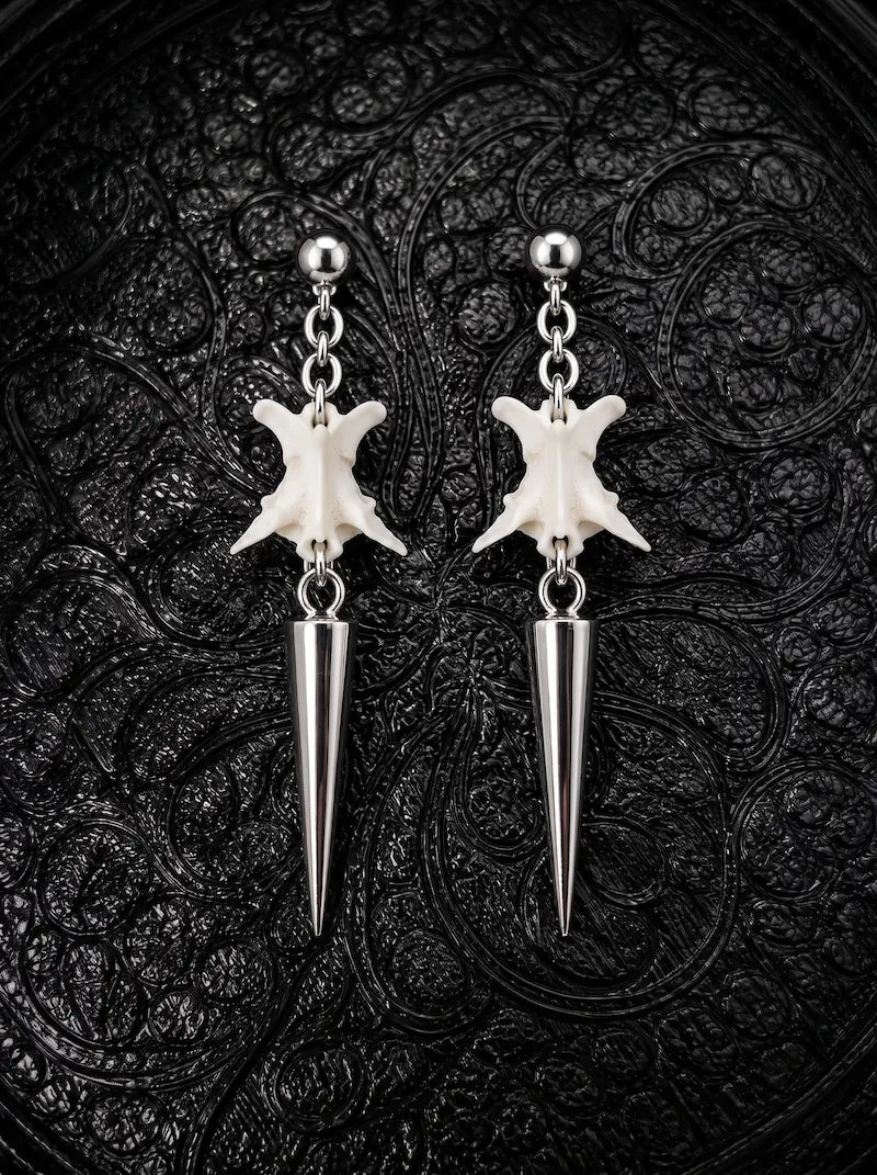Spire Chain snake bone earrings with medium-length silver-tone spikes beneath white vertebrae on black patterned fabric