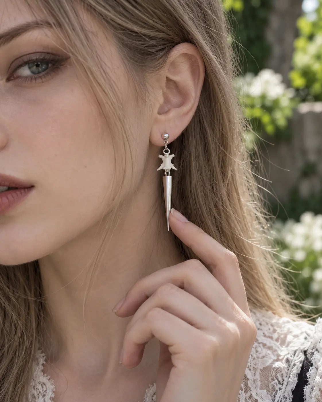 Spire Chain snake bone earring worn outdoors with a fingertip beside its pointed drop