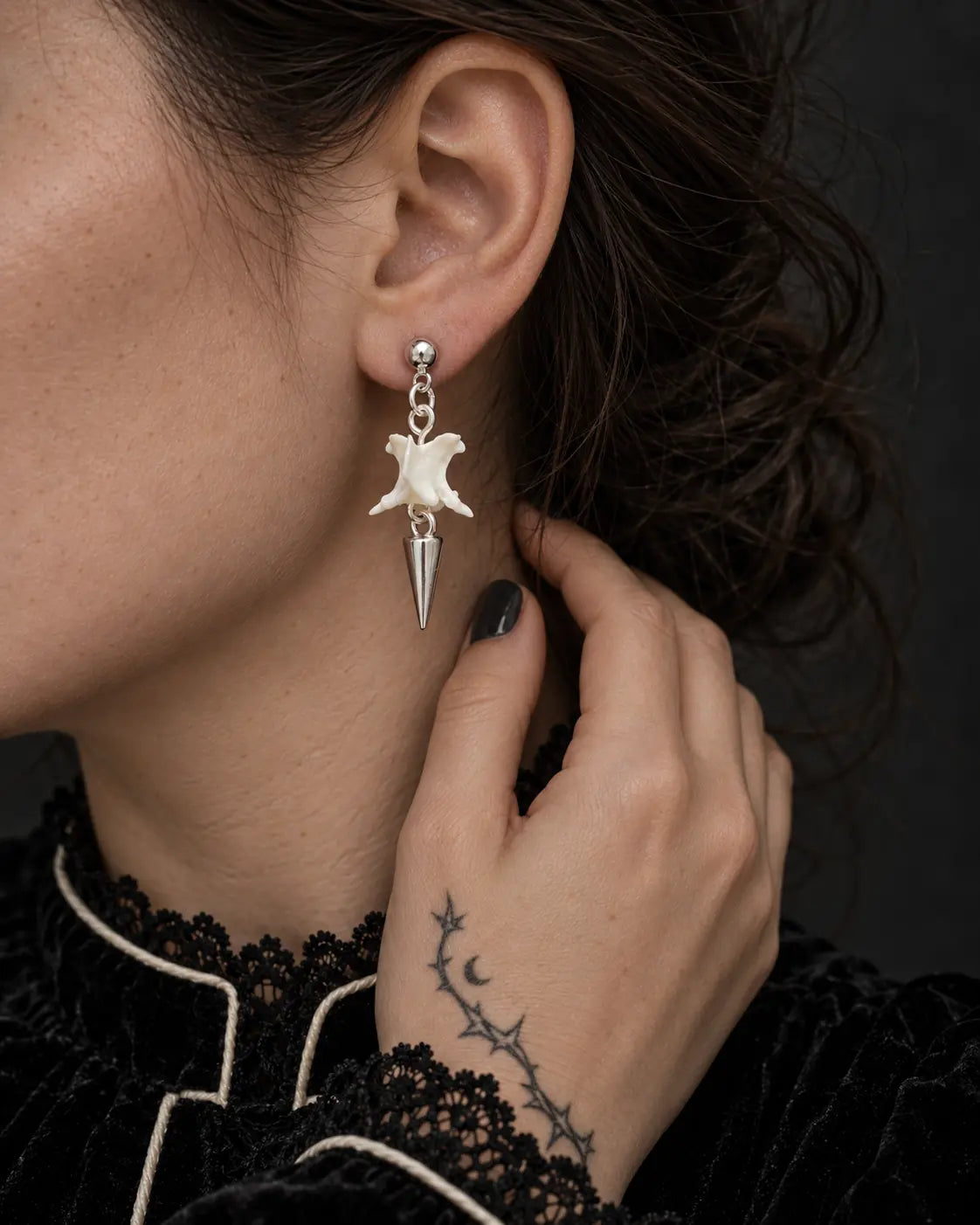 Short-spike Spire Chain snake bone earring shown beside a hand resting against the neck