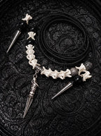 Threefold Talon snake bone necklace with black beads, three pointed metal drops and a coiled black cord on patterned fabric
