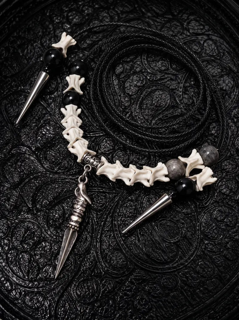 Threefold Talon snake bone necklace with black beads, three pointed metal drops and a coiled black cord on patterned fabric