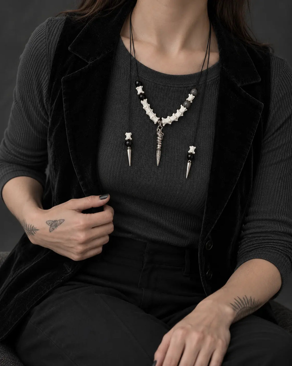 Threefold Talon snake bone necklace shown on a seated model wearing a charcoal top and black vest