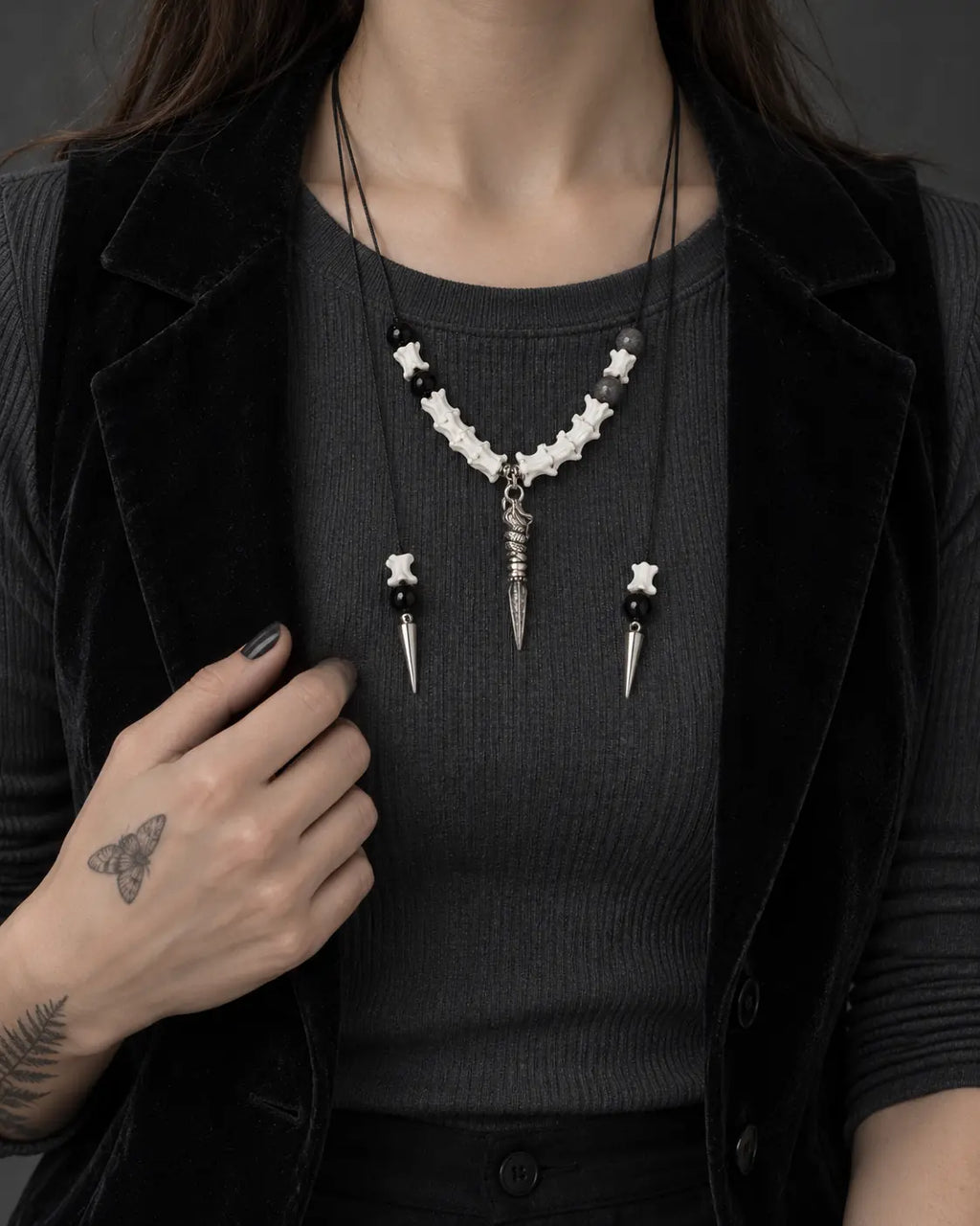 Threefold Talon snake bone necklace worn over a ribbed top with a hand holding the black vest lapel