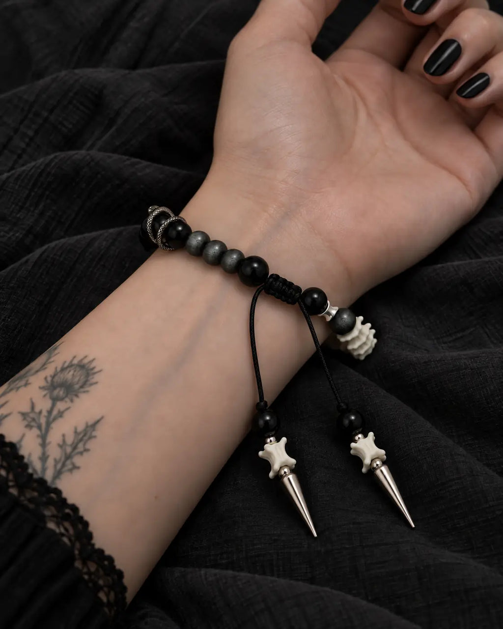 Palm-up view of the Twin Spike snake bone bracelet showing black beads, the sliding knot and two pointed drops
