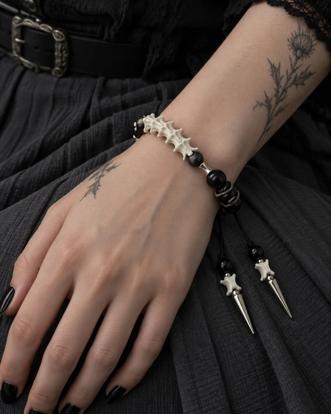 Top view of the Twin Spike snake bone bracelet on a hand resting over dark fabric