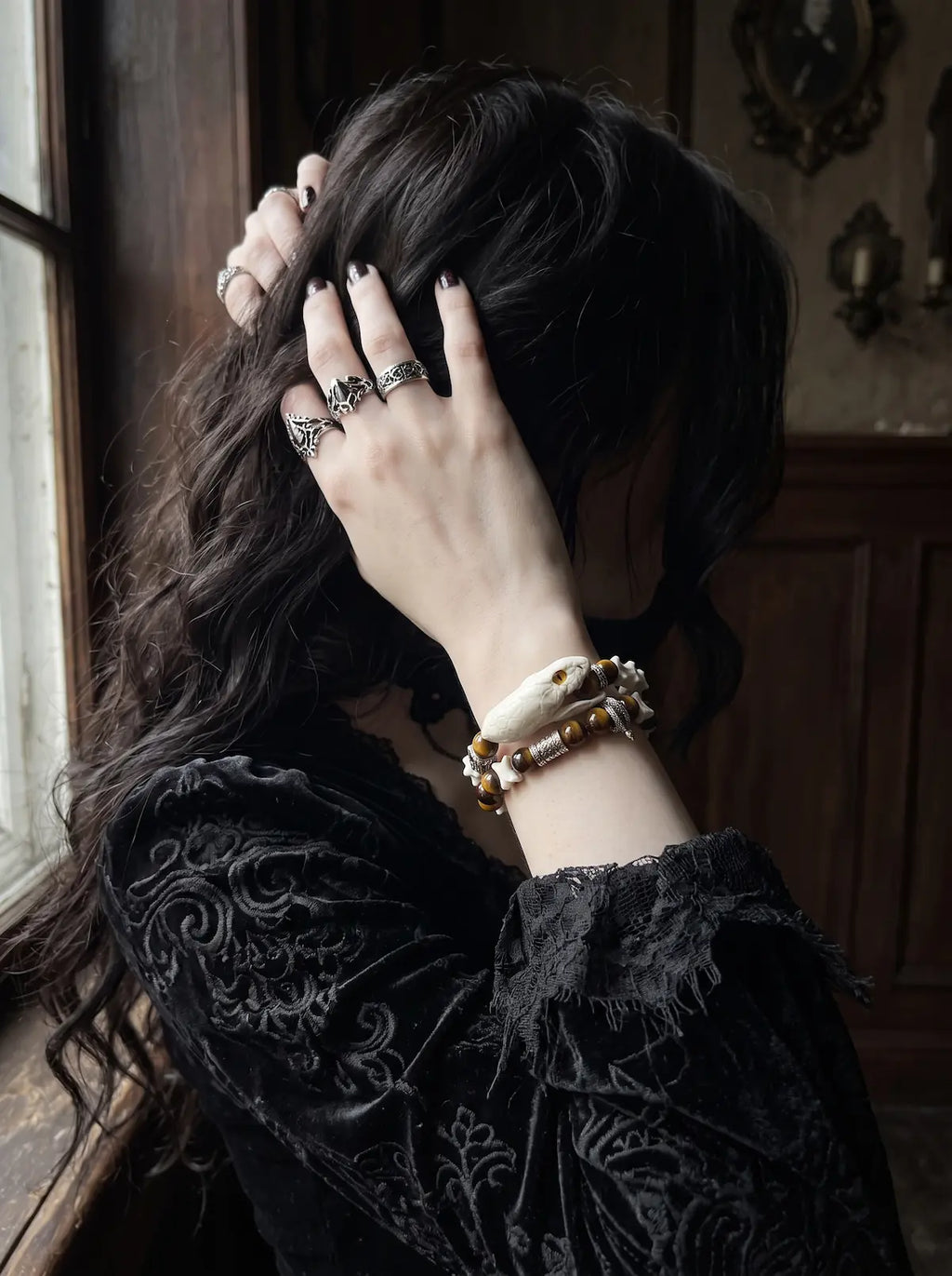 Umberblade Snake Bone Bracelet, snake bone bracelet with dark amber beads worn as a hand touches dark hair