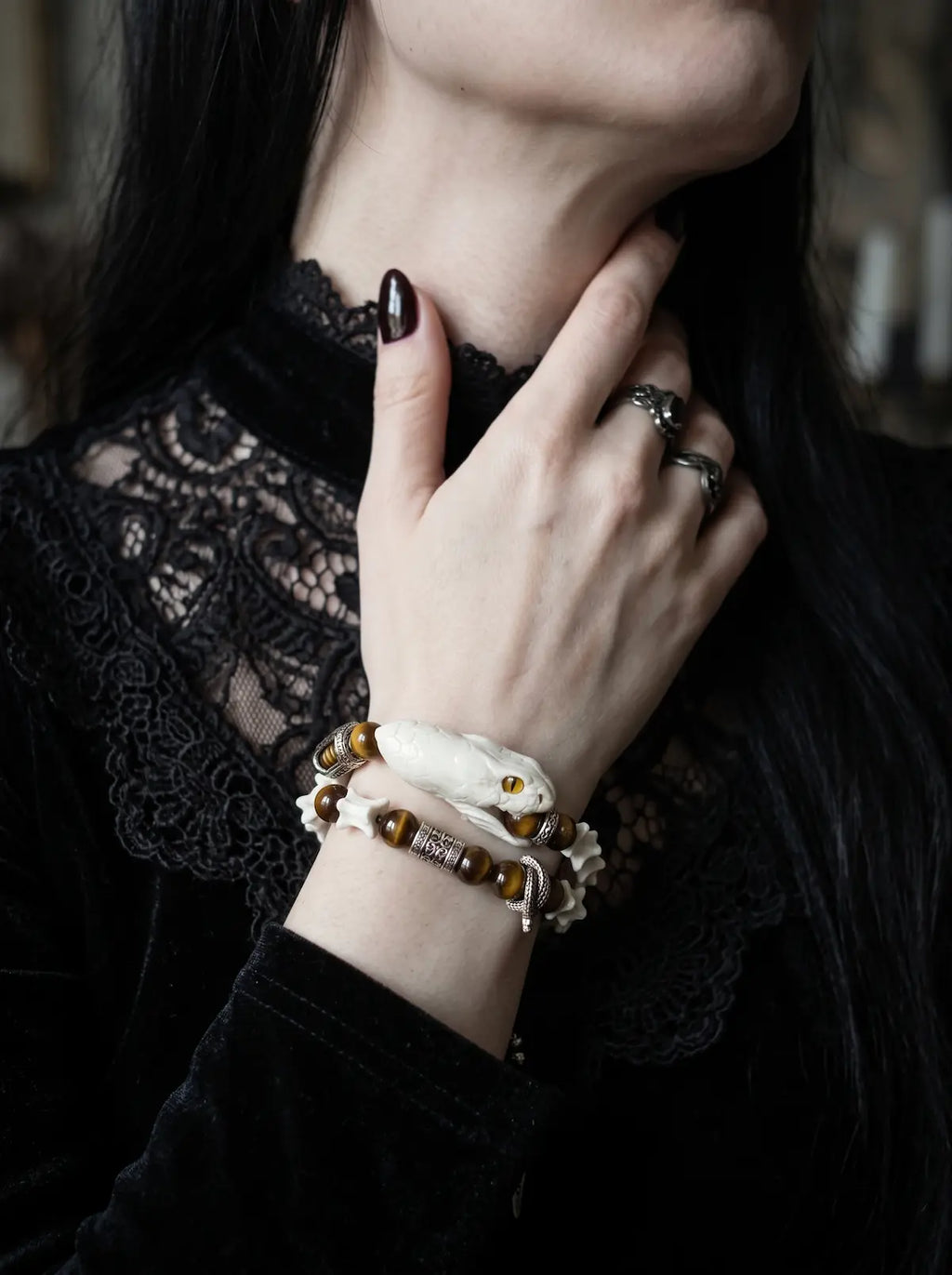 Umberblade Snake Bone Bracelet, close raised wrist view of preserved pale snake head and warm brown beads