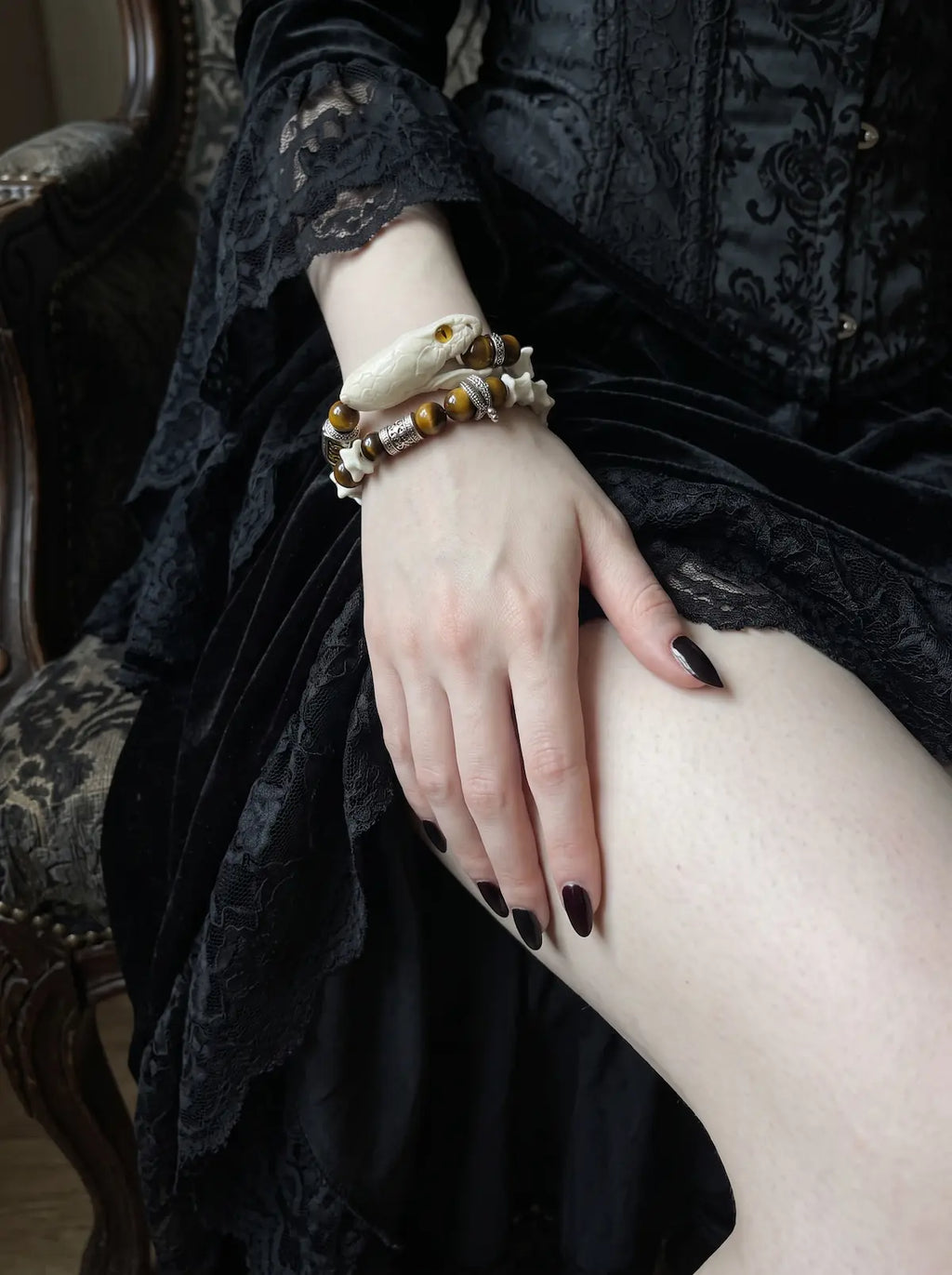 Umberblade Snake Bone Bracelet, white vertebrae and brown bead bracelet worn on a wrist above a black skirt