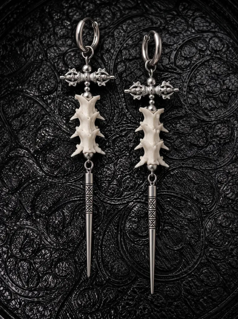 Vajra Spine snake bone earrings with ornate crossbars and long engraved silver-tone spikes on black patterned fabric