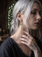 Vajra Spine snake bone earring worn beside silver-gray hair, showing its long drop against the neck