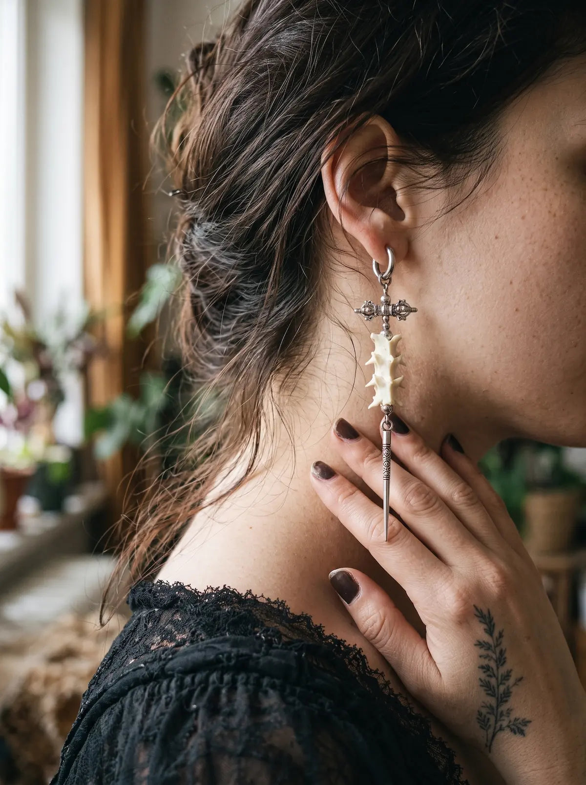 Side view of a Vajra Spine snake bone earring beside a hand resting against the neck