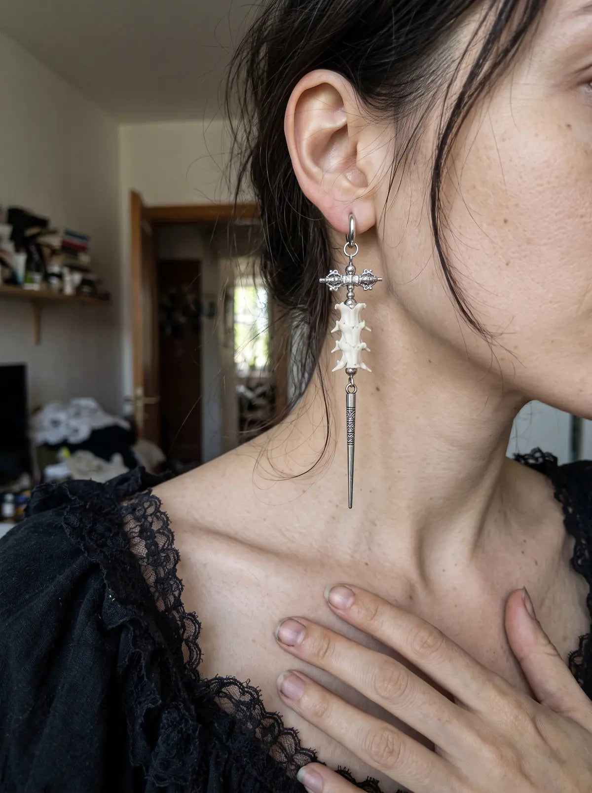 Vajra Spine snake bone earring worn with a black lace neckline and a hand resting on the chest