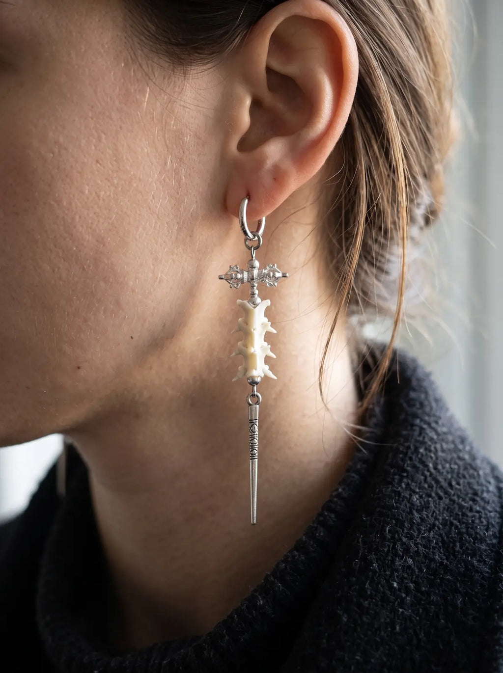 Close-up of a Vajra Spine earring showing white snake vertebrae and a long spike below the ear