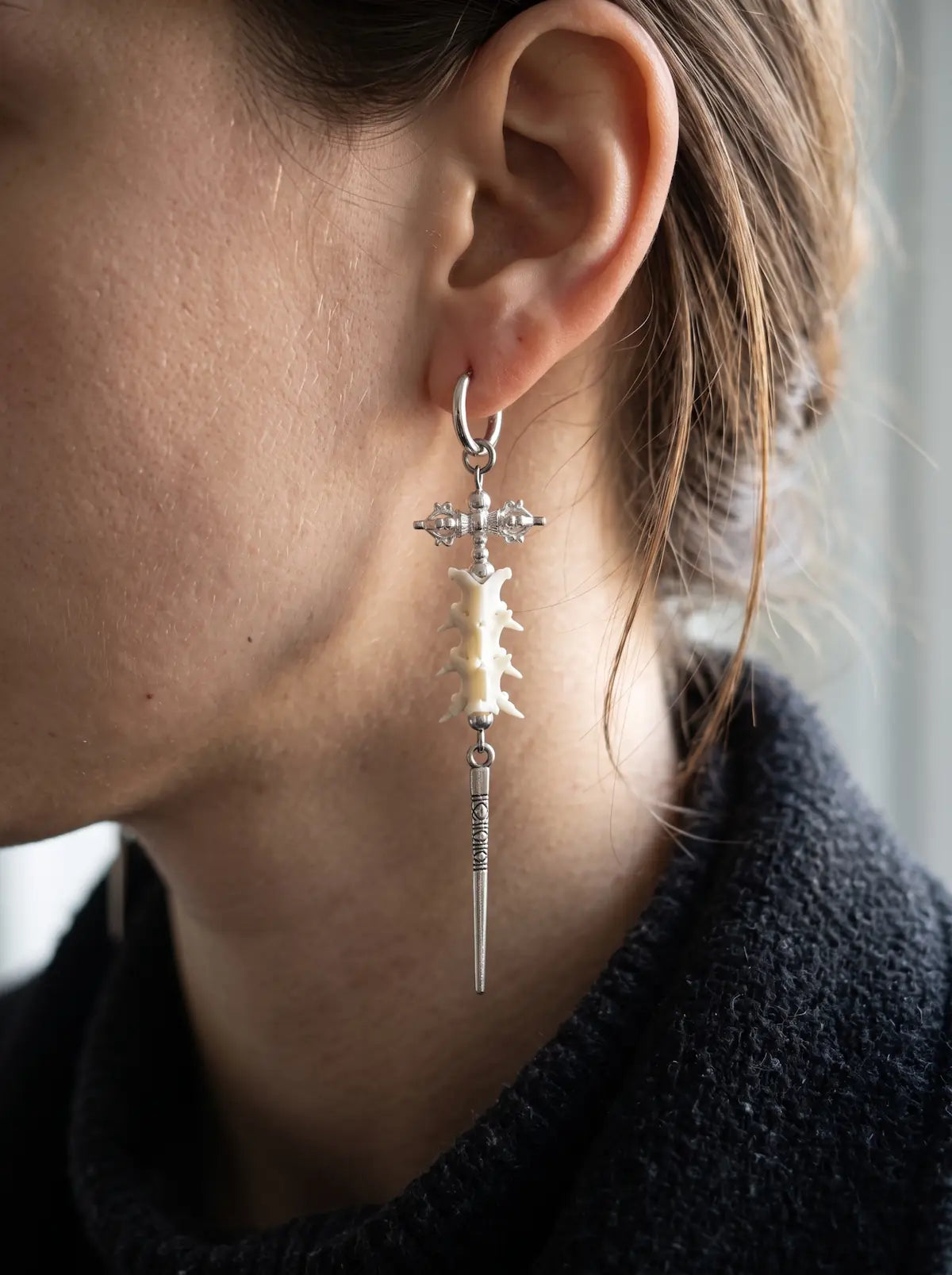 Close-up of a Vajra Spine earring showing white snake vertebrae and a long spike below the ear