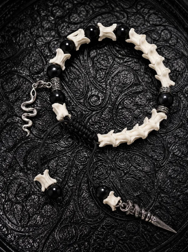 Venom Dagger snake bone bracelet with black beads, a silver-tone snake charm and a long pointed pendant on black cords