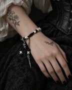 Venom Dagger snake bone bracelet worn on a hand resting against black brocade, with its snake and dagger charms visible