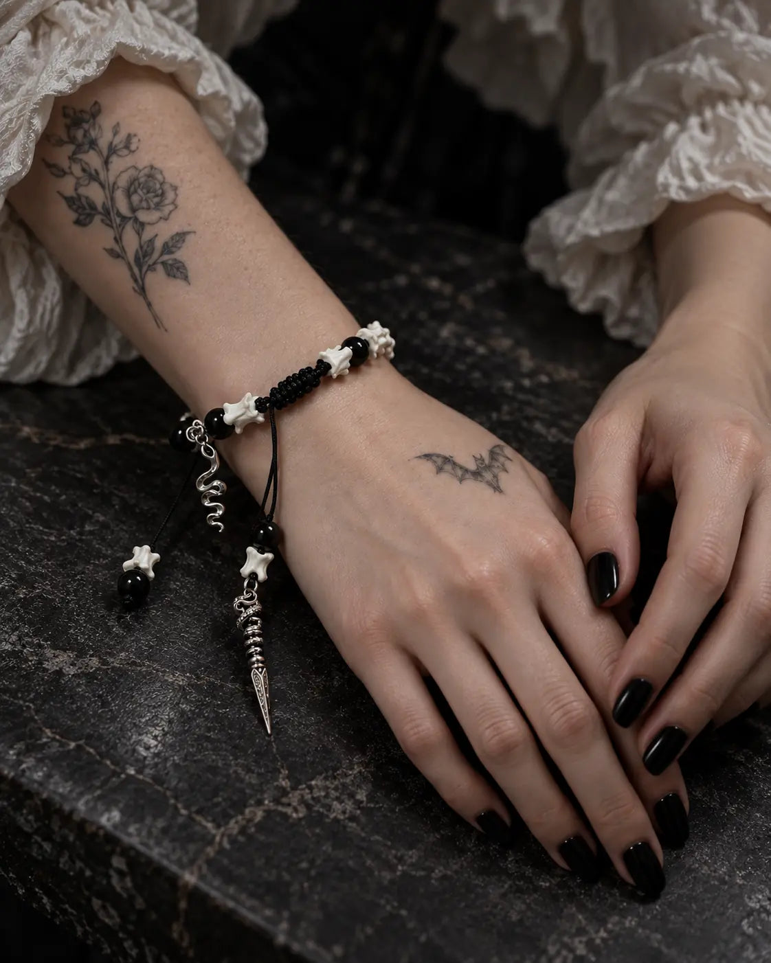 Venom Dagger snake bone bracelet on a wrist resting on a dark tabletop beside the other hand