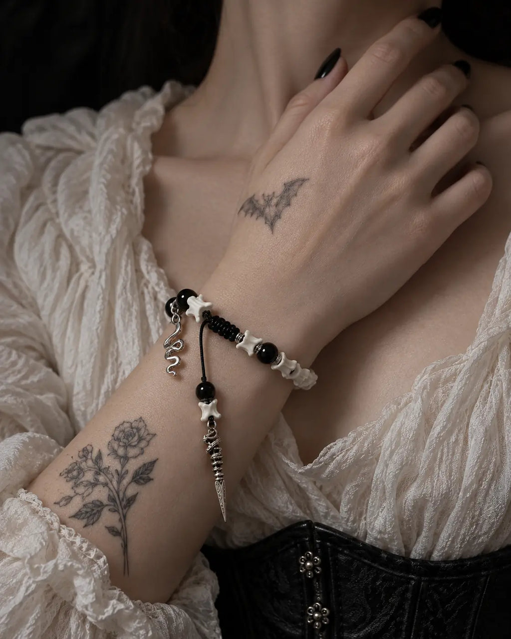 Venom Dagger snake bone bracelet worn with the hand at the collarbone above a cream blouse