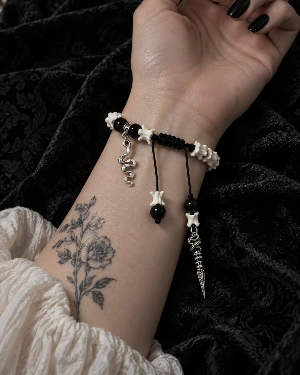 Palm-up view of the Venom Dagger snake bone bracelet showing its black braided knot and hanging charms