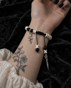 Palm-up view of the Venom Dagger snake bone bracelet showing its black braided knot and hanging charms