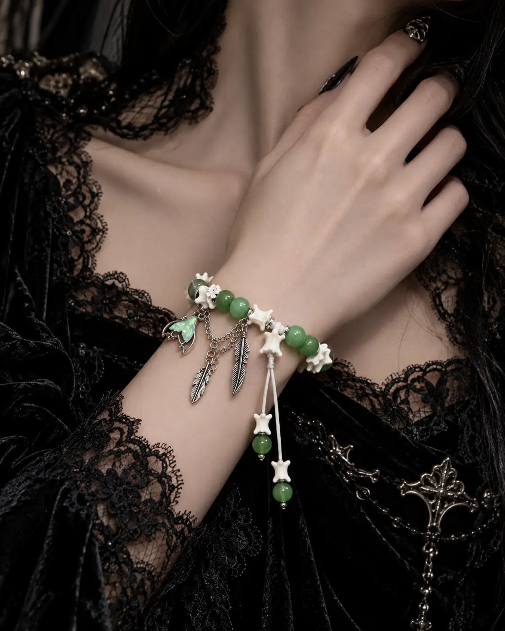 Verdant Feather snake bone bracelet worn above a black lace cuff, with its feathers and white cord ends hanging down