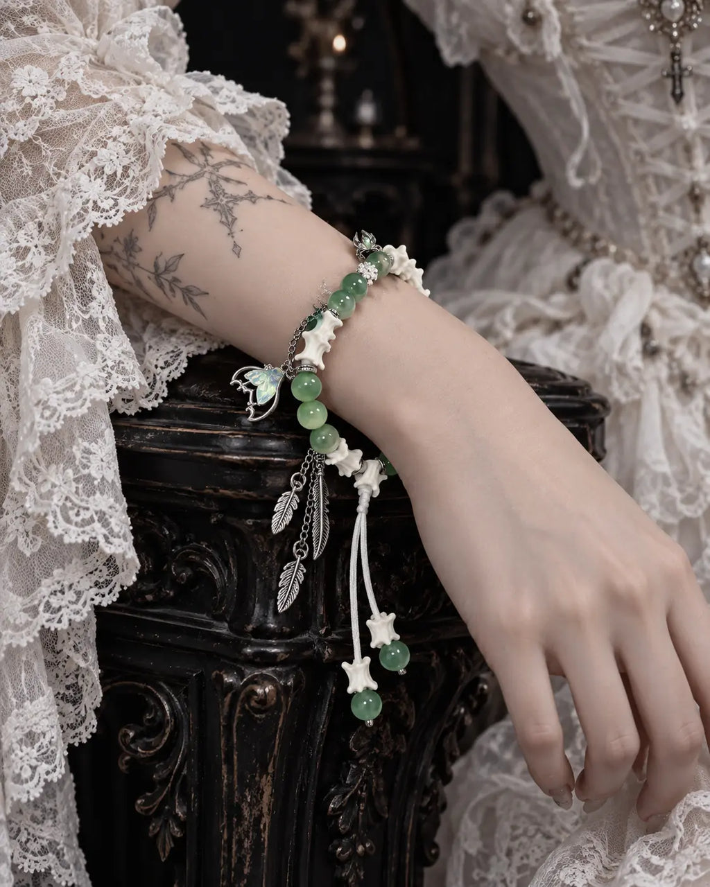 Verdant Feather snake bone bracelet on a wrist resting over carved dark furniture beside a white lace sleeve