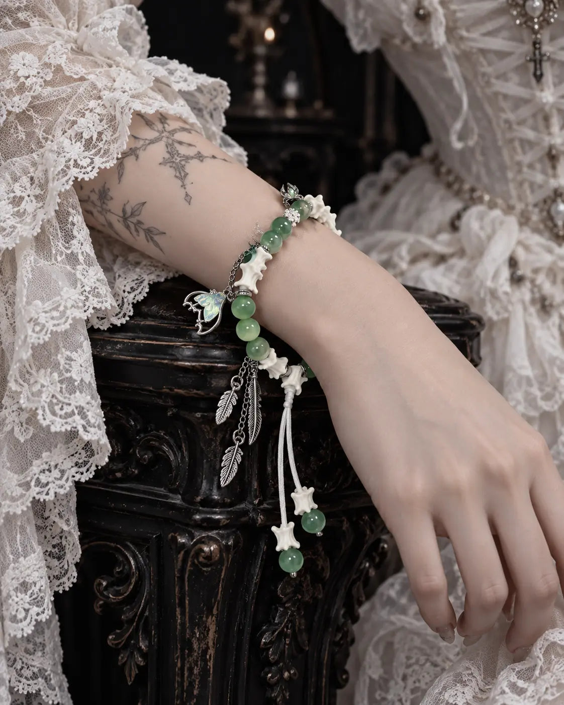 Verdant Feather snake bone bracelet on a wrist resting over carved dark furniture beside a white lace sleeve