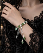 Verdant Feather snake bone bracelet on a raised wrist above black velvet, with an iridescent wing and feather drops