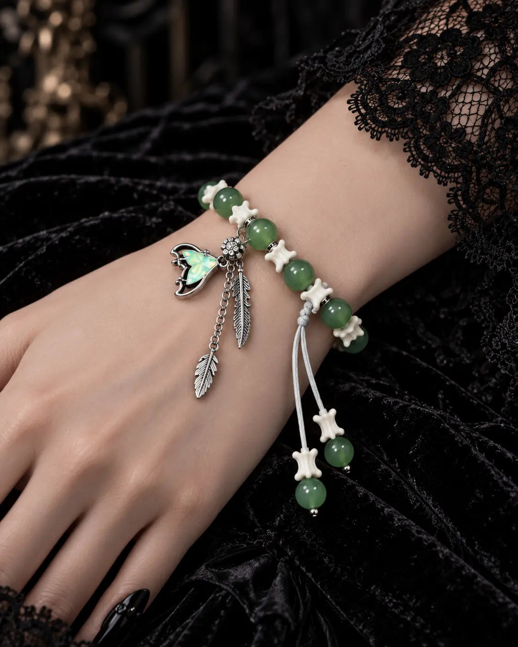 Close-up of the Verdant Feather snake bone bracelet showing green beads, three feather charms and bone-tipped white cords