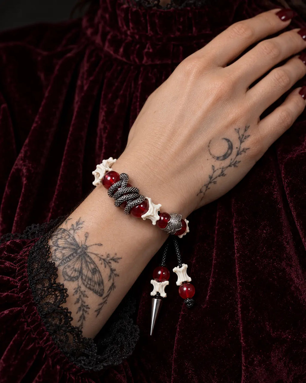 Vermilion Fang snake bone bracelet worn against burgundy velvet, highlighting its serpent-wrapped red bead