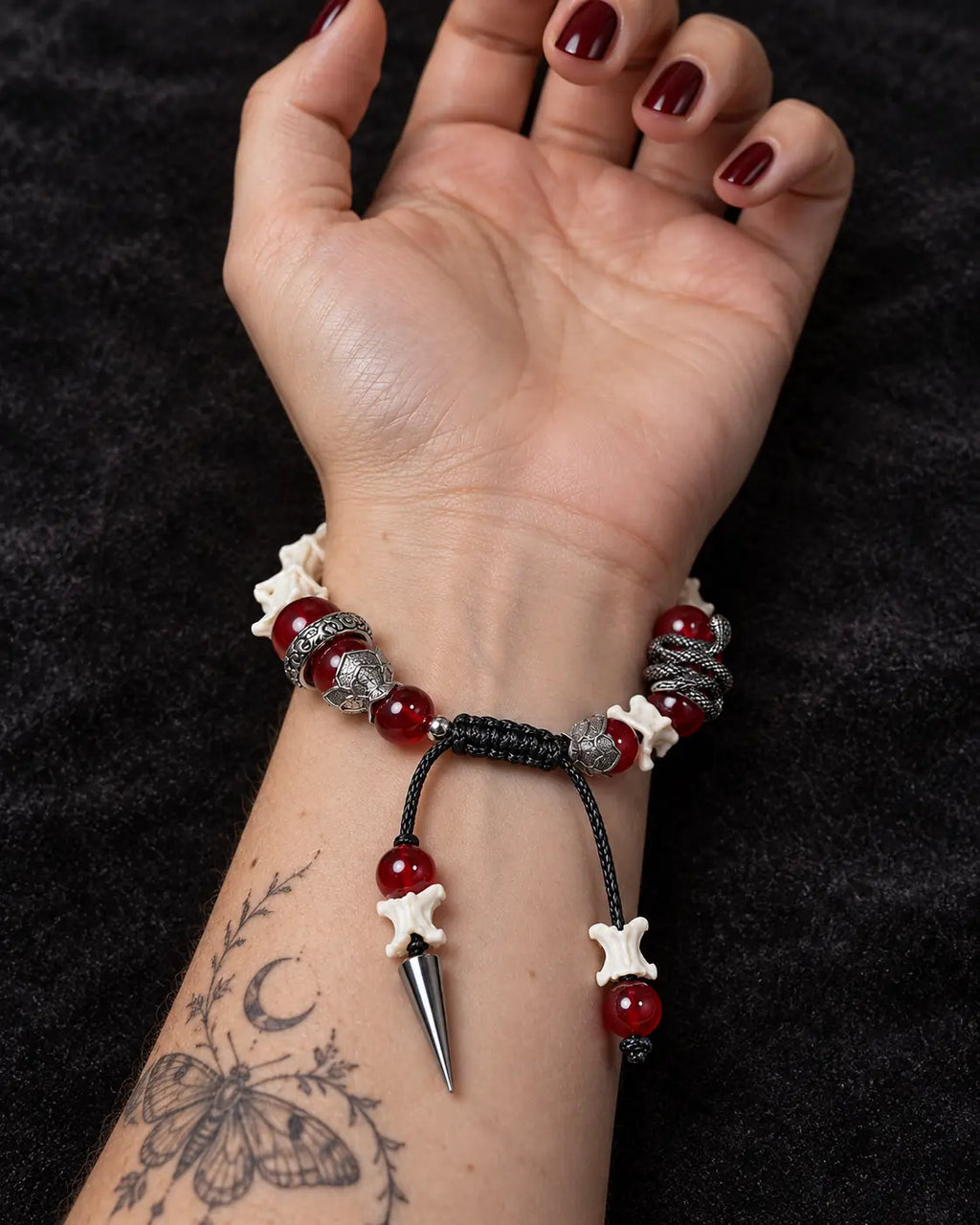 Palm-up view of the Vermilion Fang snake bone bracelet showing red beads, a black sliding knot and a spike drop