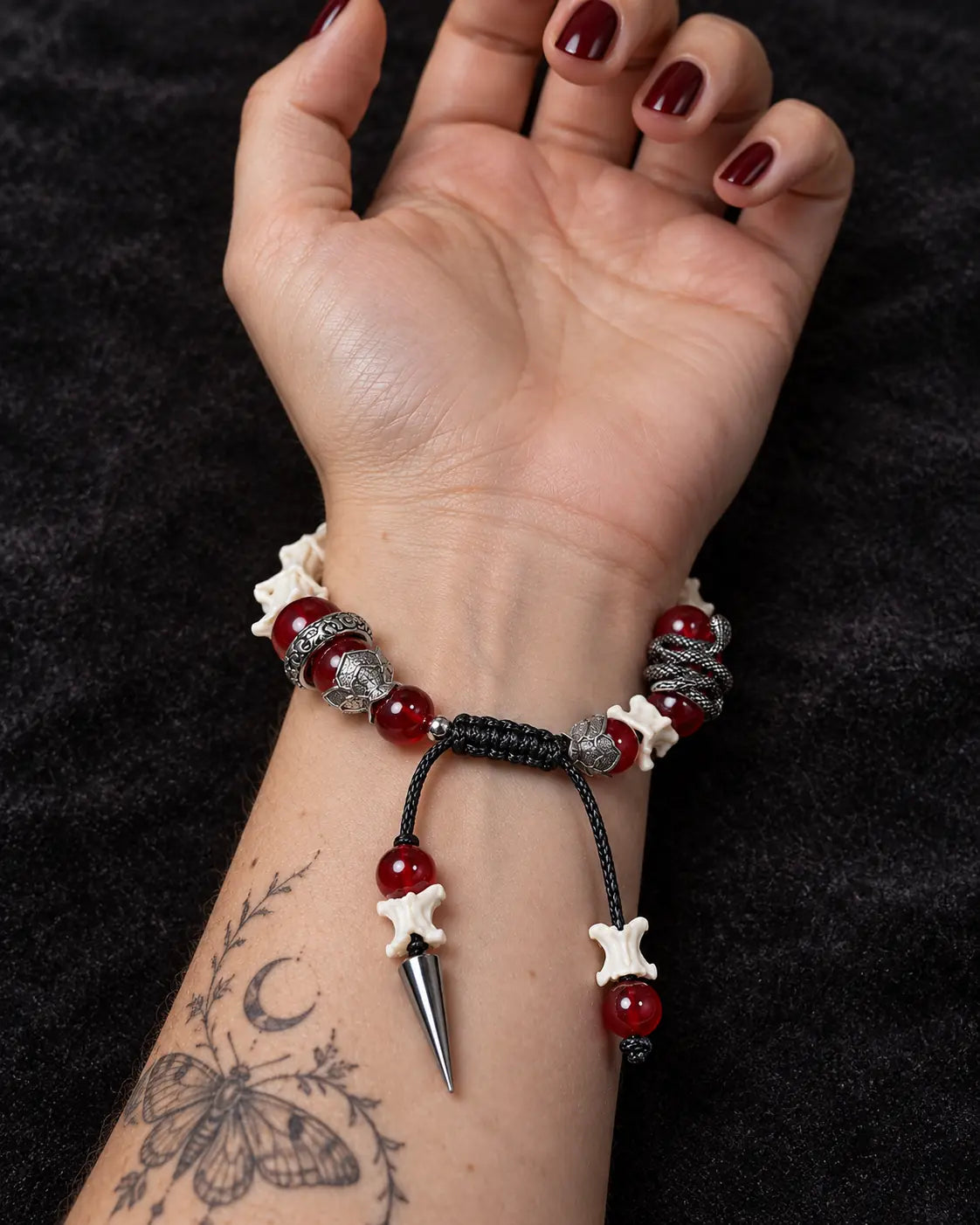 Palm-up view of the Vermilion Fang snake bone bracelet showing red beads, a black sliding knot and a spike drop