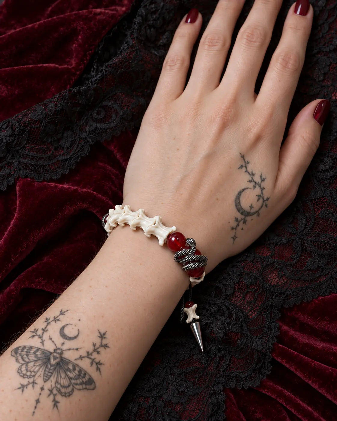 Vermilion Fang snake bone bracelet on a hand resting against burgundy velvet and black lace