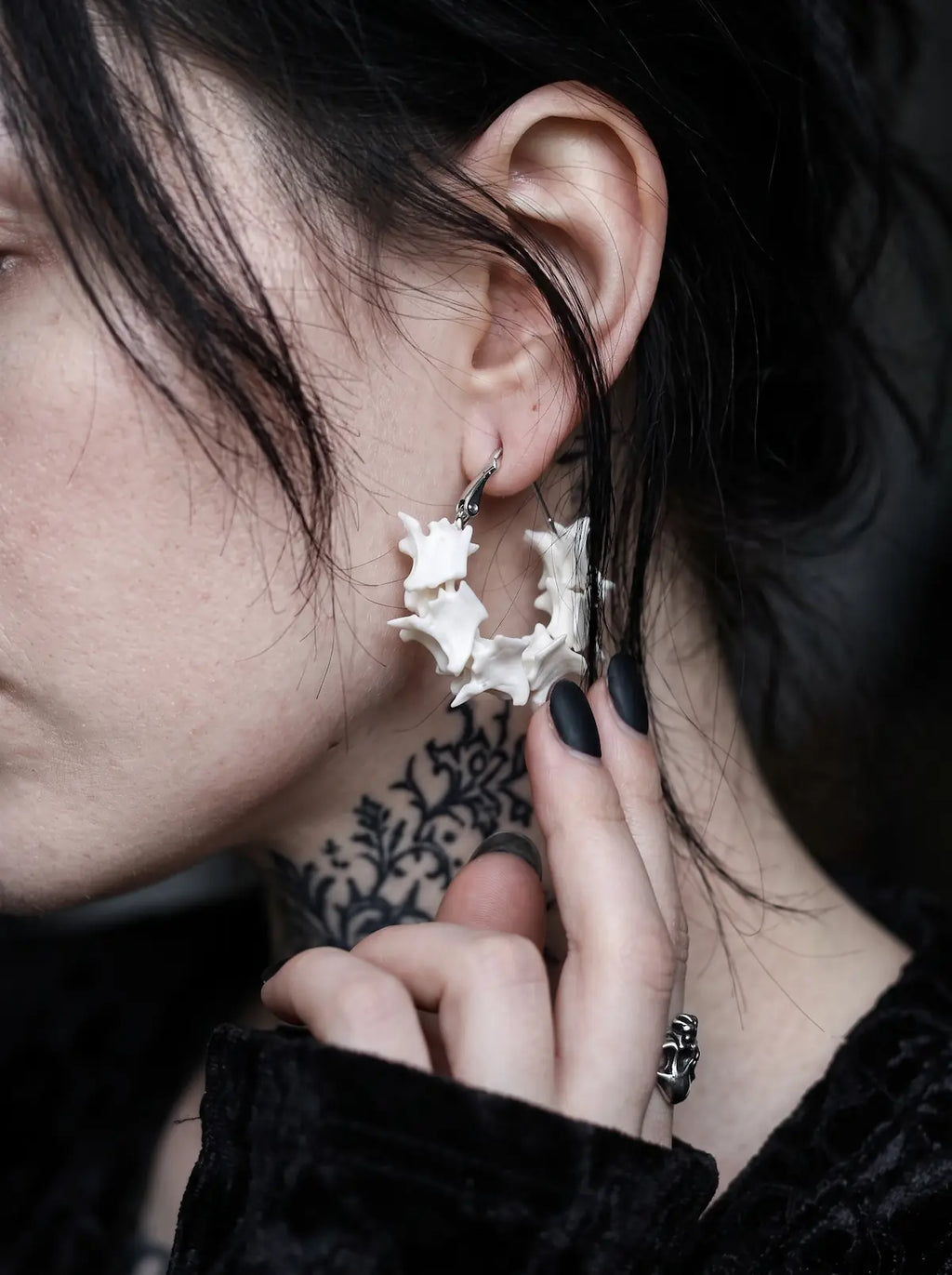 Close-up side view of a Vertebra Crescent snake bone earring with a fingertip below the curved bones
