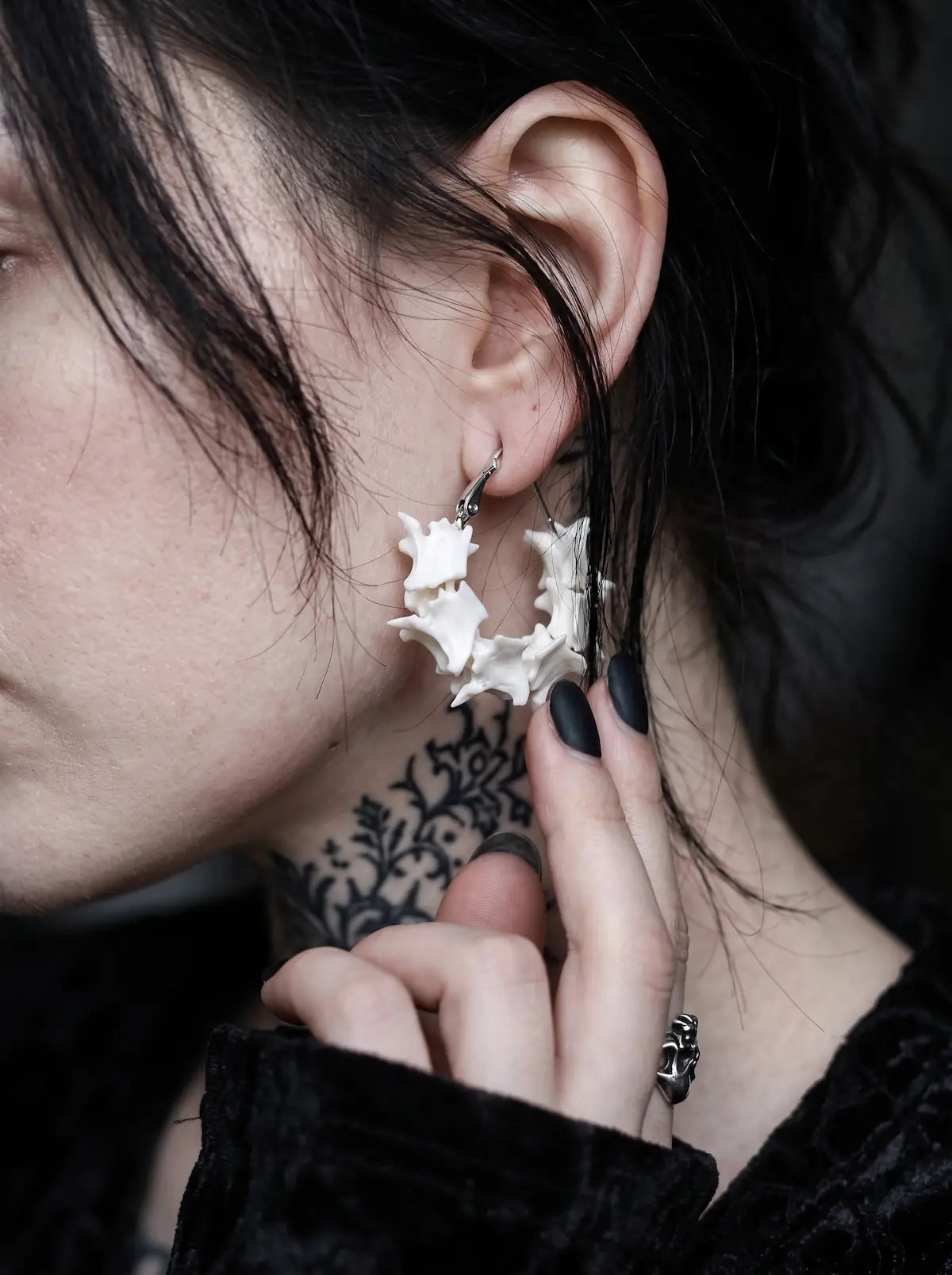 Close-up side view of a Vertebra Crescent snake bone earring with a fingertip below the curved bones