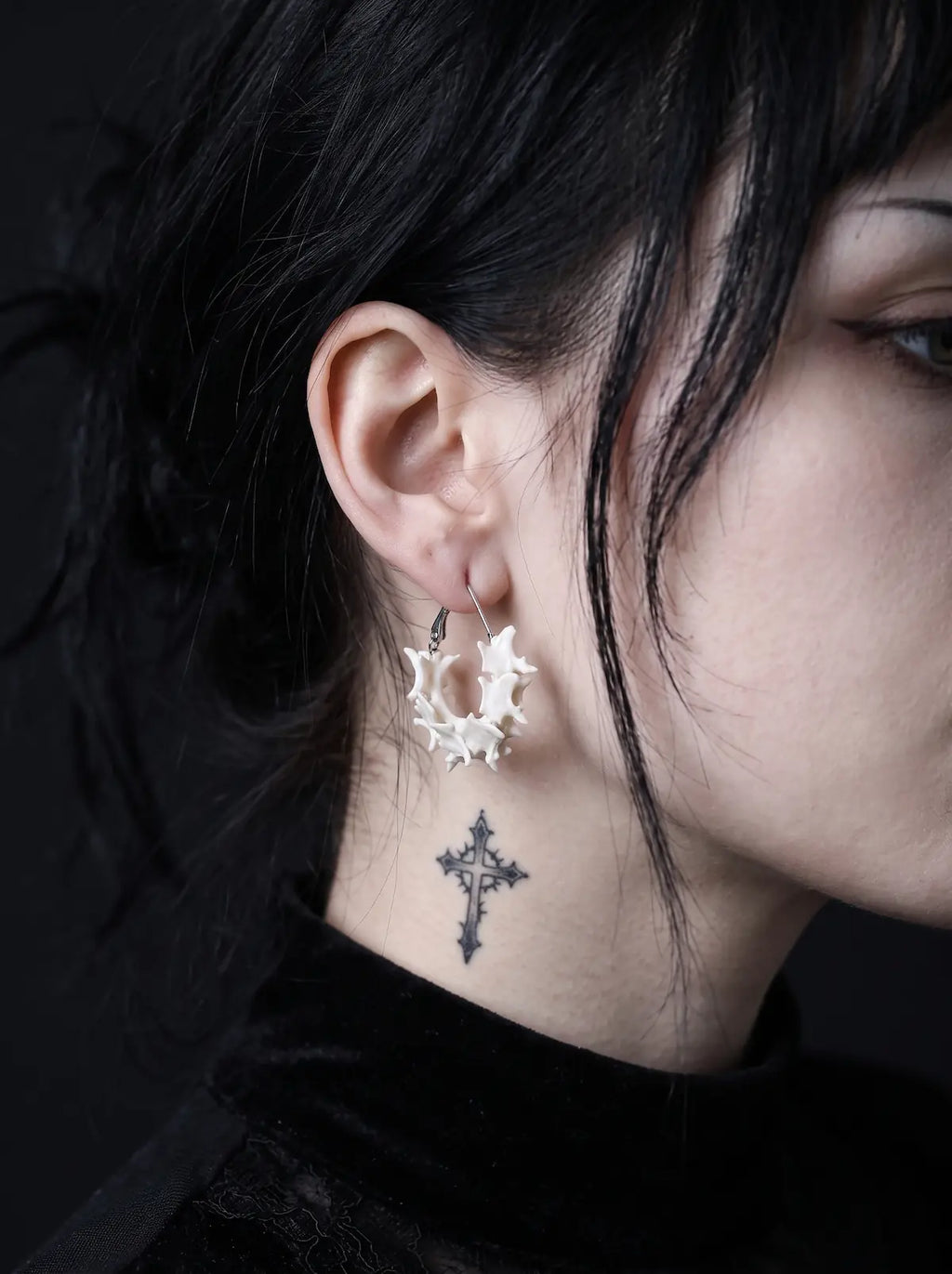 Vertebra Crescent snake bone earring shown in profile above a cross tattoo on the neck