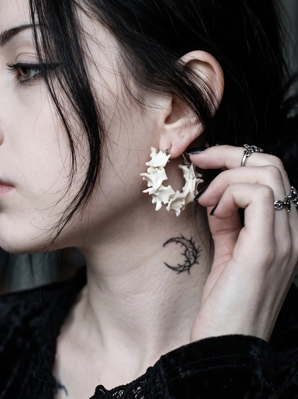 Vertebra Crescent snake bone earring worn with a ringed hand lifting the hair beside the ear