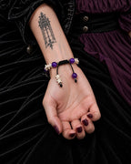 Palm-up view of the Violet Dragon snake bone bracelet showing its black sliding knot and bone- and bead-tipped cords