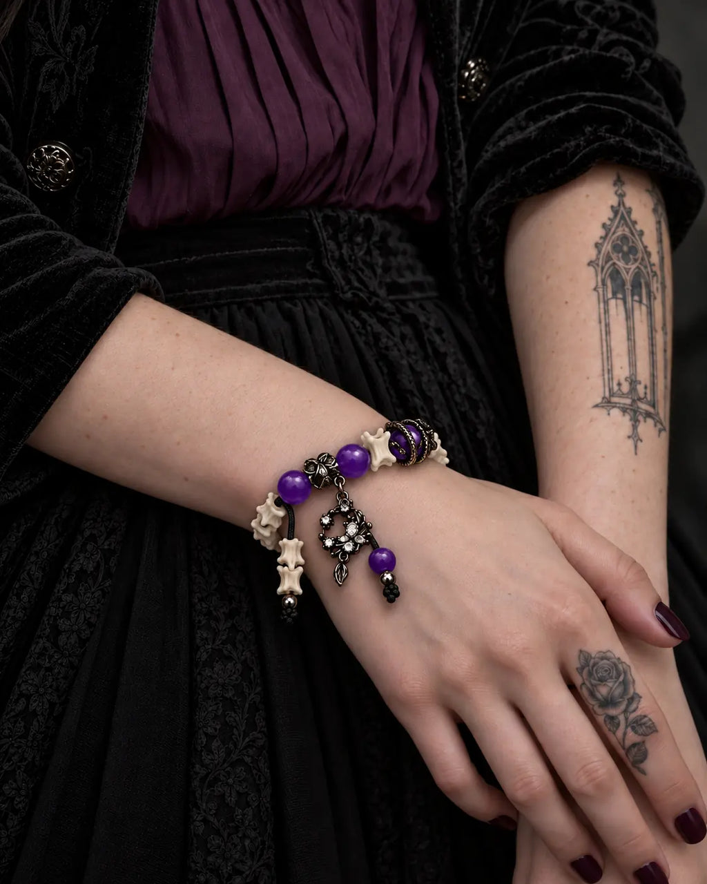 Violet Dragon snake bone bracelet worn with one hand resting across the opposite wrist over a purple dress