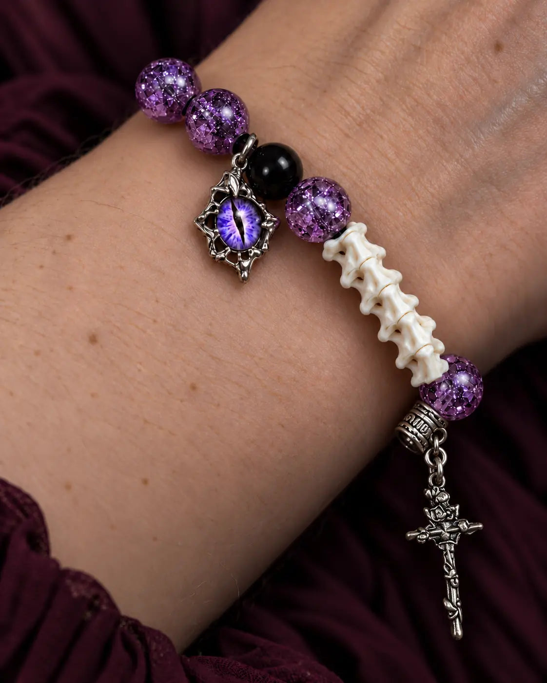 Close-up of the Violet Serpent Eye snake bone bracelet showing its purple eye charm, crackled beads and cross drop