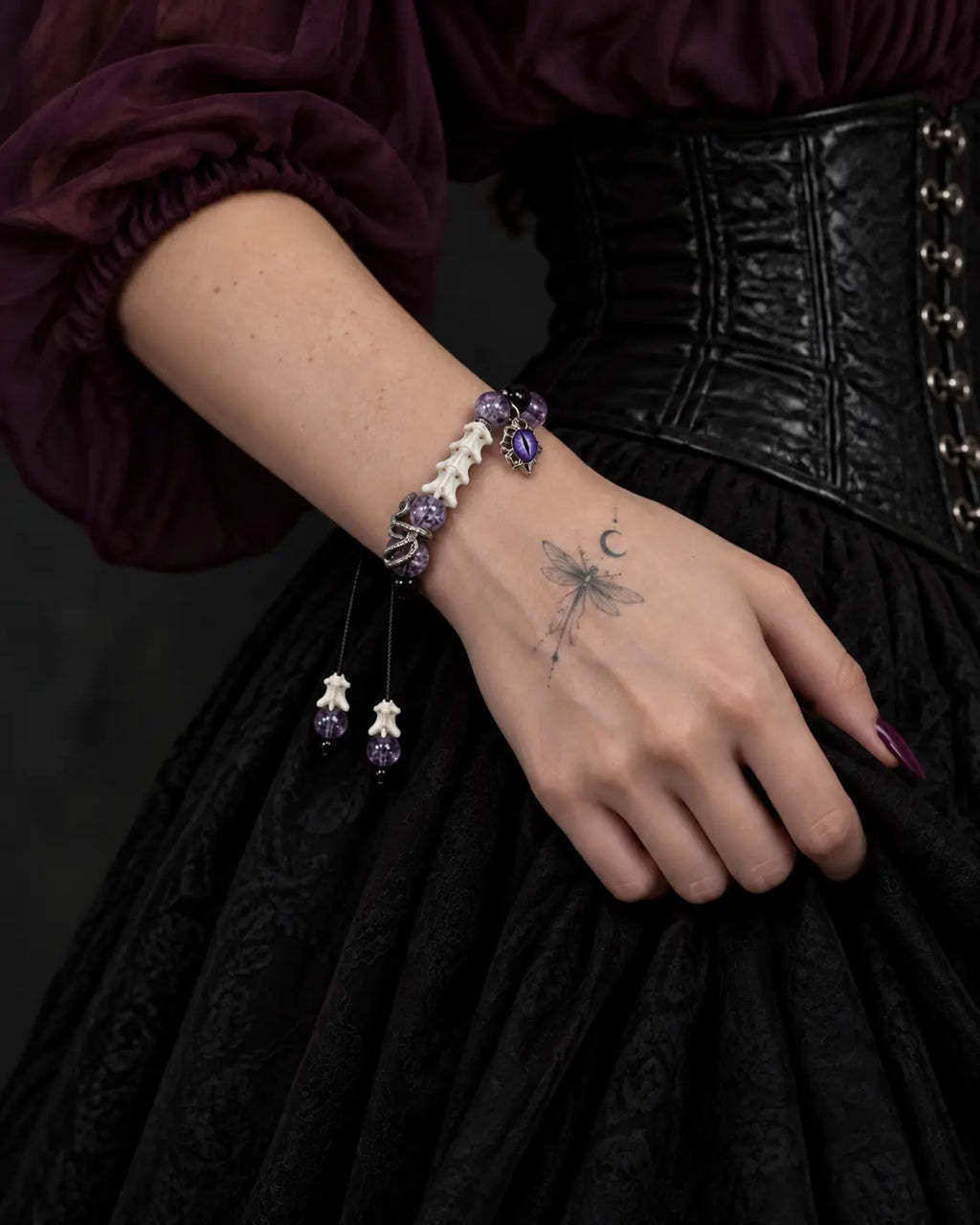 Violet Serpent Eye snake bone bracelet worn on a wrist against a black skirt beneath a purple sleeve