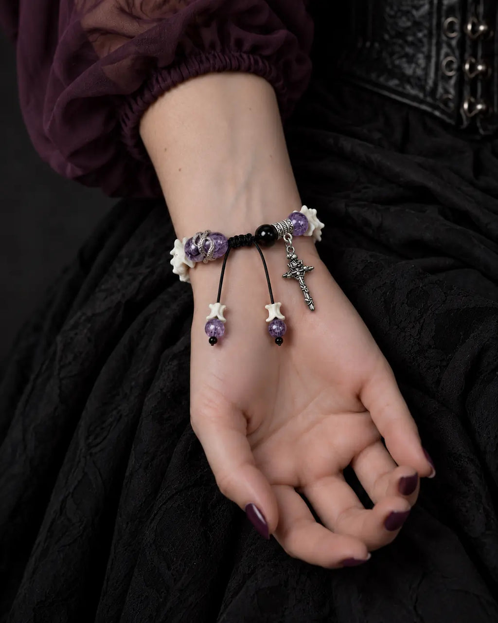 Palm-up view of the Violet Serpent Eye snake bone bracelet showing its black sliding knot, cross and beaded cord ends
