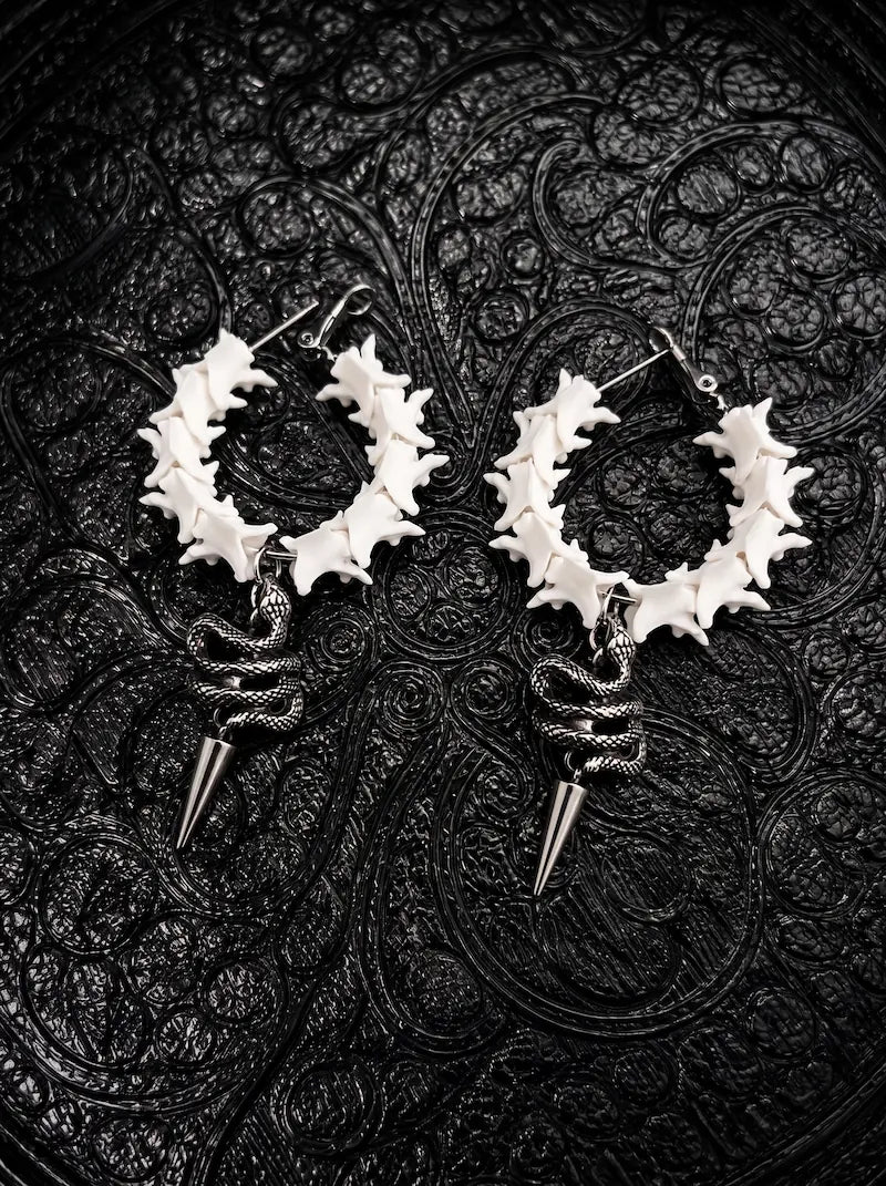 Viper Drop snake bone hoop earrings with coiled serpent accents and pointed silver-tone drops on black patterned fabric