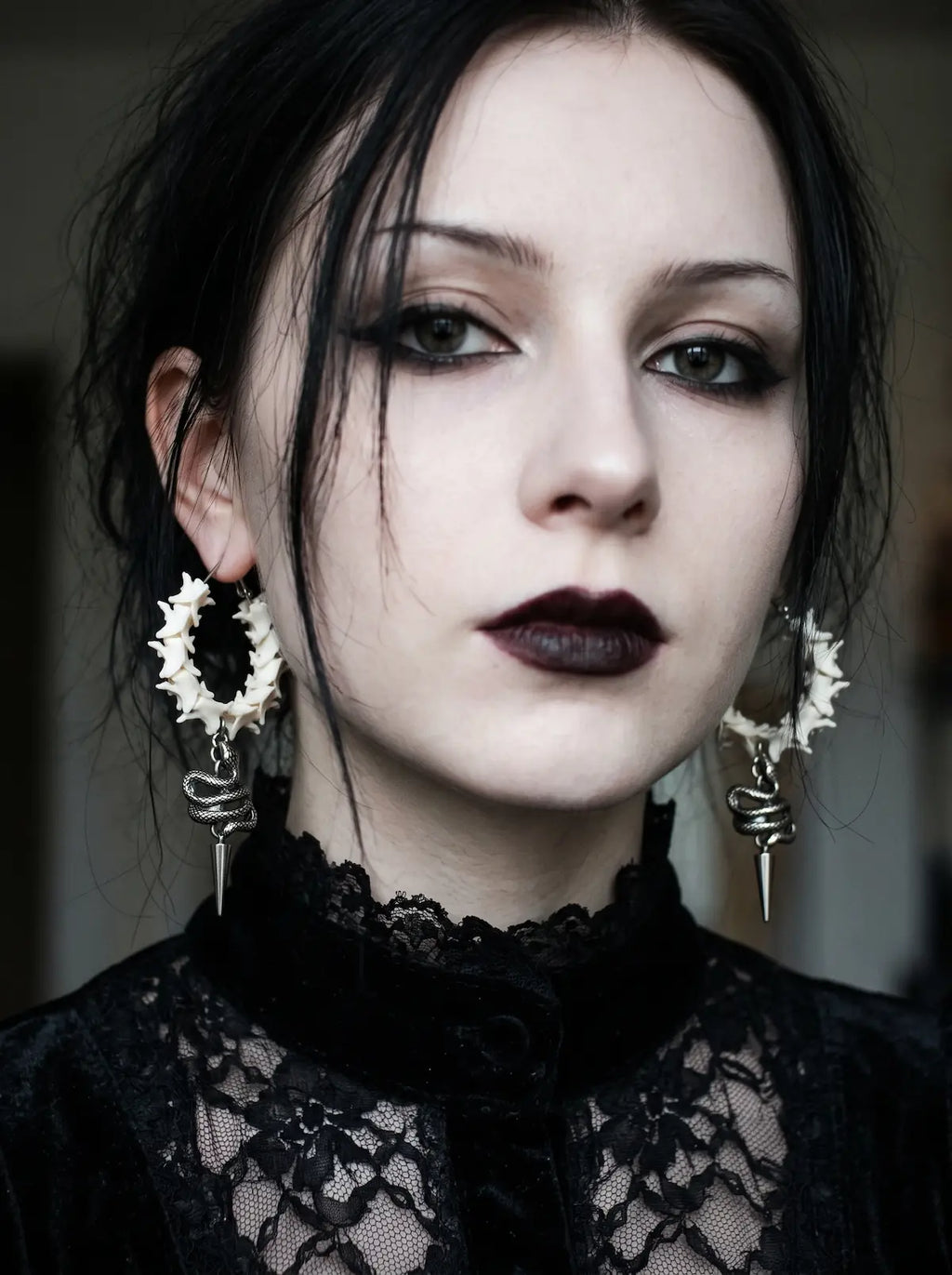 Viper Drop snake bone earrings worn as a pair above a high black lace neckline