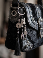 Yin Talisman Snake Bone Keychain, close detail of metal coins and pale vertebrae keychain on a black shoulder bag