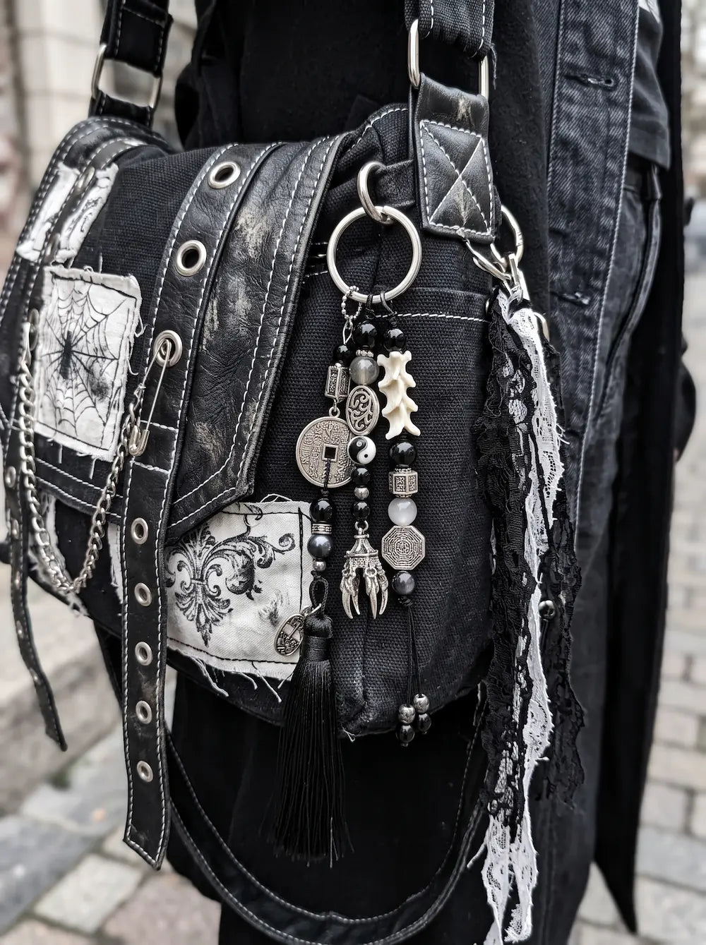 Yin Talisman Snake Bone Keychain, black tassel and coin charm keychain clipped to a patterned gothic-style bag